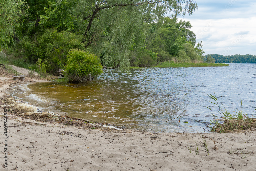 Sandy beach with spring view on picturesque river on natural park. Trees and plants water edge with green rivershore. Landscape with lush foliage and dense grove near water. Atmospher in reserve. Sandy beach with spring view on picturesque river on natural park. Trees and plants water edge with green rivershore. Landscape with lush foliage and dense grove near water. Atmospher in reserve.