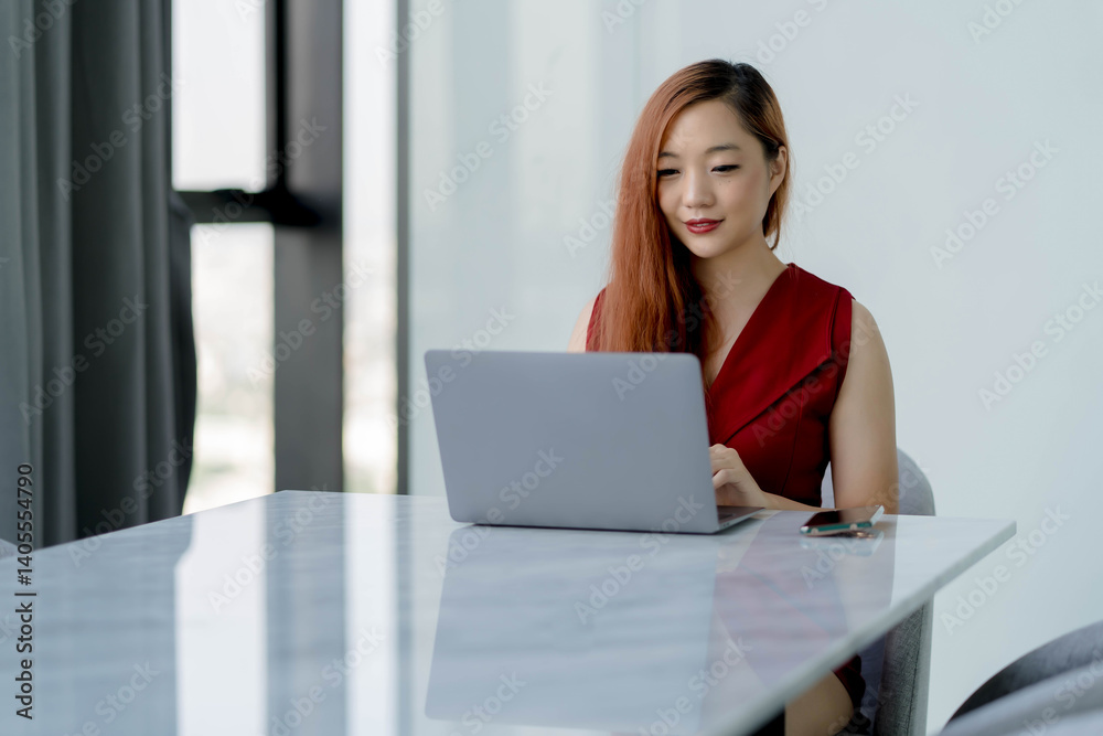 Confident Asian businesswoman working on laptop in bright modern office with marble table, wearing red dress and smiling while using technology for business tasks Confident Asian businesswoman working on laptop in bright modern office with marble table, wearing red dress and smiling while using technology for business tasks