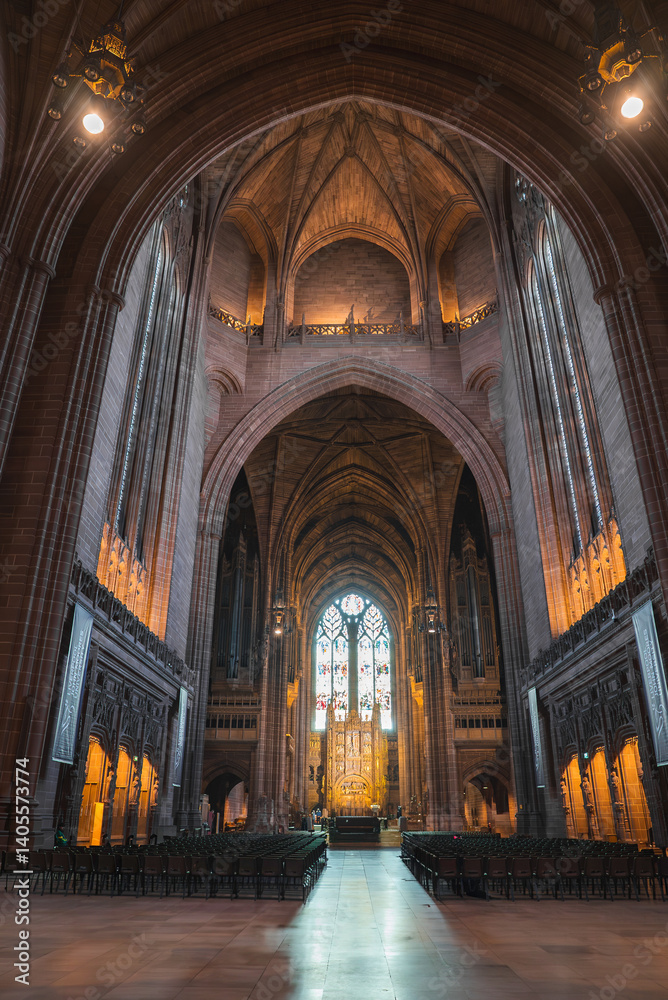 The grand interior of Liverpool Cathedral features soaring Gothic arches, intricate stonework, a stained glass window, and rows of neatly arranged chairs.