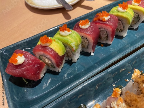 A close-up, top-down view showcases two rows of beautifully crafted sushi rolls on a textured blue plate.