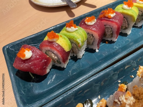 A close-up, top-down view showcases two rows of beautifully crafted sushi rolls on a textured blue plate.