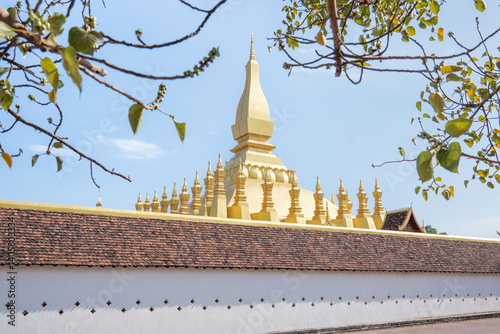 That Luang Stupa in Vientiane, Laos, shining brightly under a clear blue sky during the Lao New Year festival. The golden landmark represents national pride, peace, and spiritual heritage