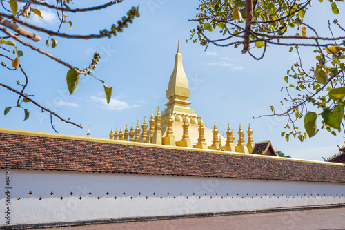 That Luang Stupa in Vientiane, Laos, shining brightly under a clear blue sky during the Lao New Year festival. The golden landmark represents national pride, peace, and spiritual heritage
