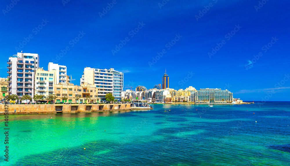 Cityscape of St Julian's Bay on a sunny day with clear blue skies and turquoise water, Malta