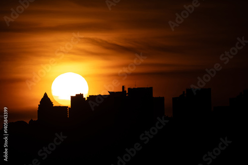 The Kyiv skyline at dusk showcases the Pechersk district silhouetted against the fading light, with various buildings distinguishable on the right bank. photo