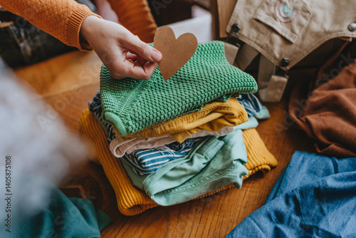 Close-up of woman holding a paper heart near an old out-of-use kid clothes for charity or upcycling