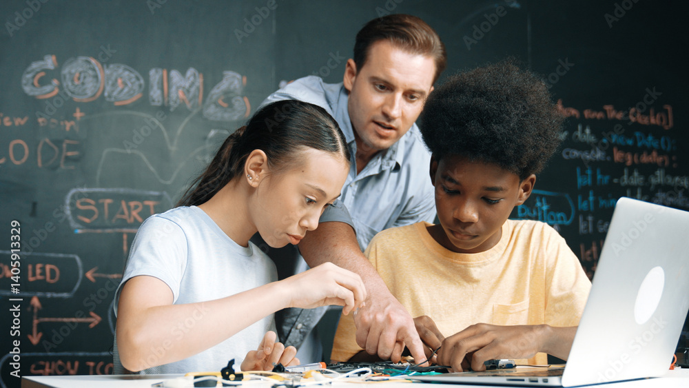 Caucasian teacher talking about electric tool while student fixing robotic model on table with electronic equipment placed. Diverse academic children learning about main board structure. Edification.