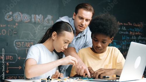 Obraz na płótnie Caucasian teacher talking about electric tool while student fixing robotic model on table with electronic equipment placed. Diverse academic children learning about main board structure. Edification. w salonie