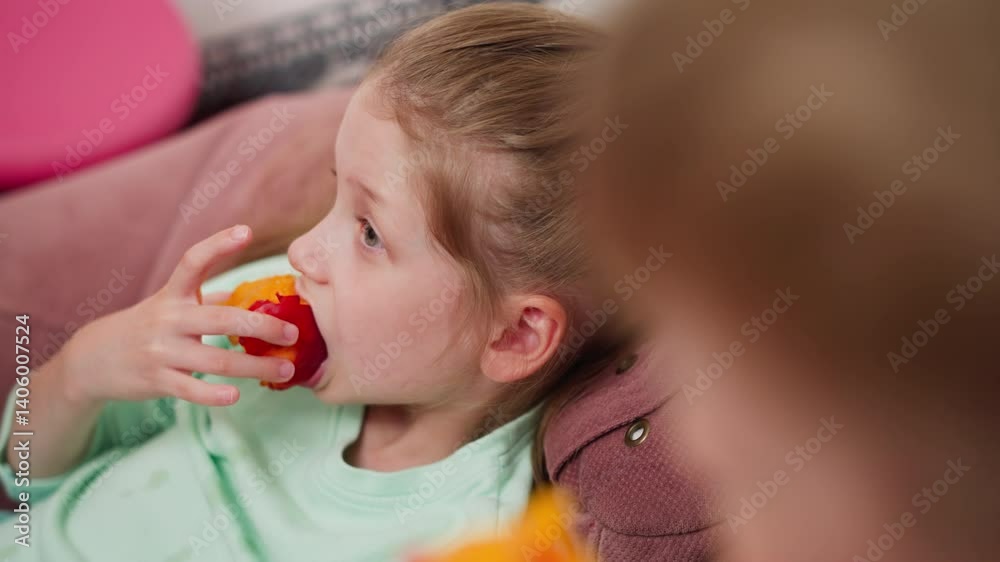 Close up of boy playfully showing sister juicy mango as girl looks at his fruit then happily takes big bite from her own vibrant mango while relaxing on cozy bean bag in brightly lit cheerful room Close up of boy playfully showing sister juicy mango as girl looks at his fruit then happily takes big bite from her own vibrant mango while relaxing on cozy bean bag in brightly lit cheerful room