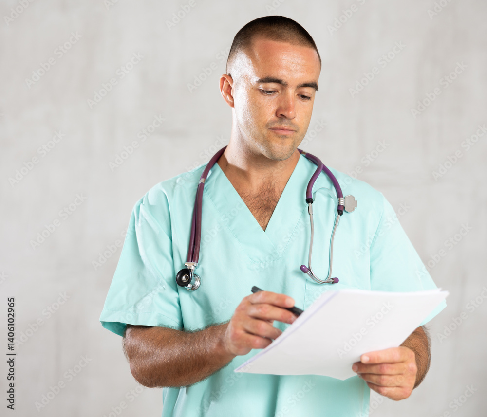 Portrait of male doctor in medical gown with stethoscope making notes in the patient medical history Portrait of male doctor in medical gown with stethoscope making notes in the patient medical history