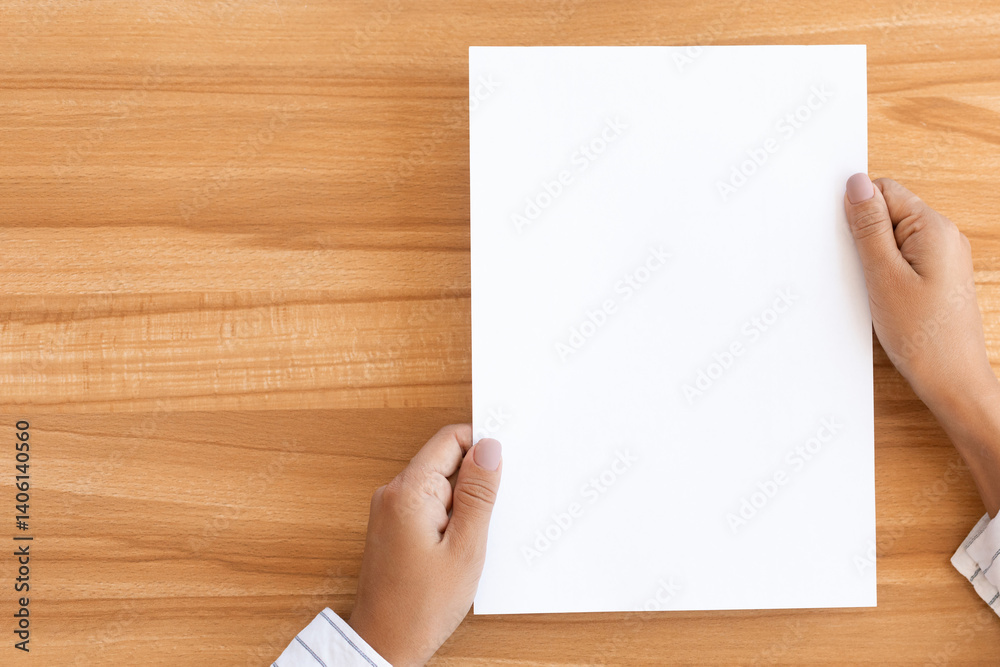 Overhead view of woman holding blank paper sheet A4 size or letter paper on wooden desk background, copy space Overhead view of woman holding blank paper sheet A4 size or letter paper on wooden desk background, copy space