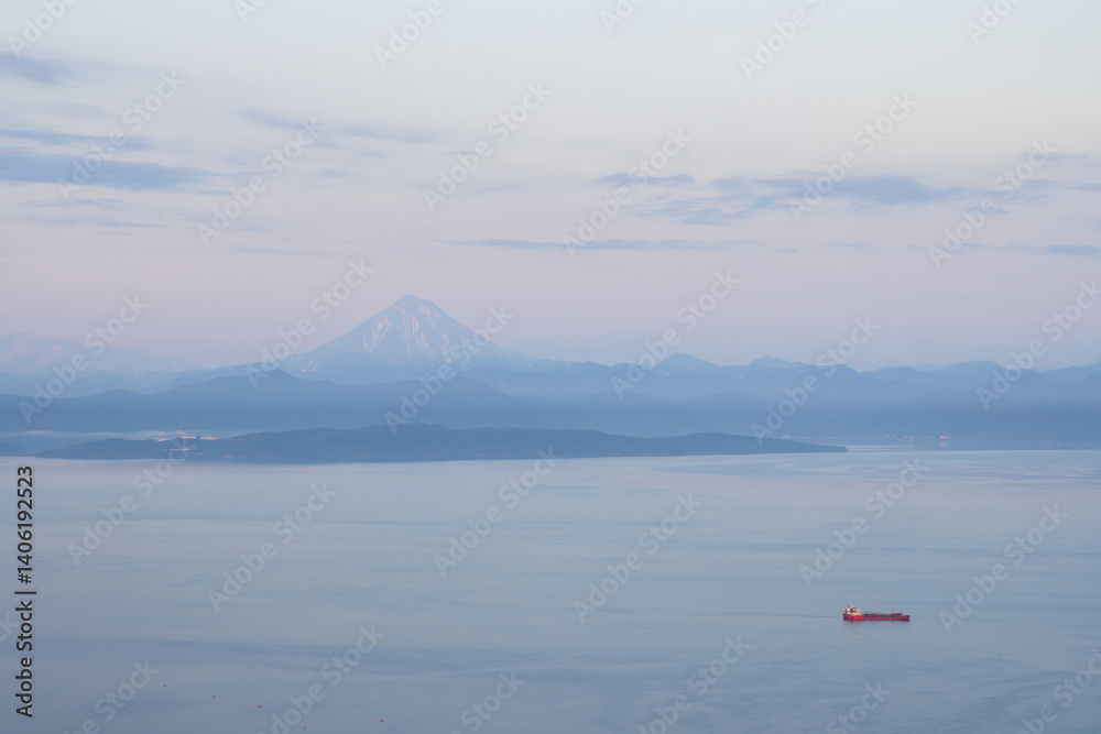 Beautiful morning landscape. View of the cargo ship in the bay. Mountains and Vilyuchinsky volcano in the distance. Avacha Bay, Pacific Ocean. Kamchatka Territory, Far East of Russia.
