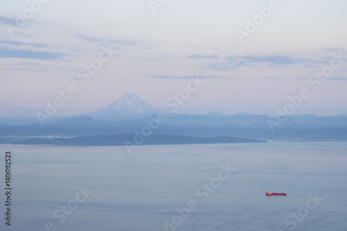 Obraz na płótnie Beautiful morning landscape. View of the cargo ship in the bay. Mountains and Vilyuchinsky volcano in the distance. Avacha Bay, Pacific Ocean. Kamchatka Territory, Far East of Russia. w salonie