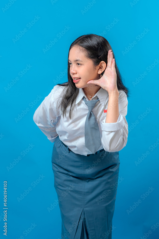 Cheerful Indonesian high school girl in uniform with expressive face and curious look, cupping her ear to listen carefully. Great concept for communication or awareness campaigns. Cheerful Indonesian high school girl in uniform with expressive face and curious look, cupping her ear to listen carefully. Great concept for communication or awareness campaigns.
