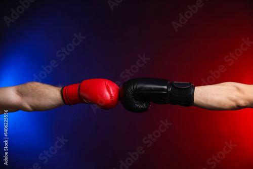 Men with boxing gloves fighting on dark background in neon lights, closeup