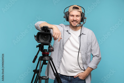 Man with professional video camera and headset on light blue background
