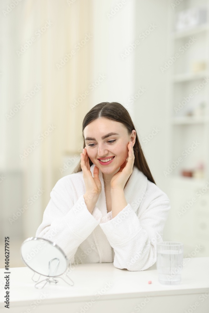 Smiling woman looking at round mirror and glass of collagen water on table indoors Smiling woman looking at round mirror and glass of collagen water on table indoors