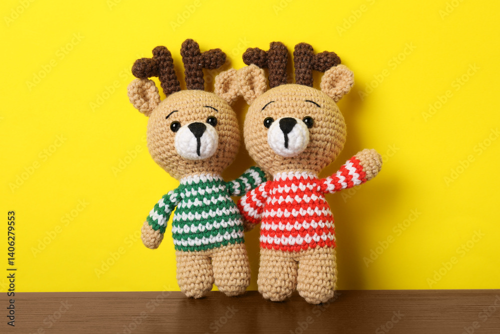 Fototapeta premium Cute knitted toy deers on wooden table against yellow background