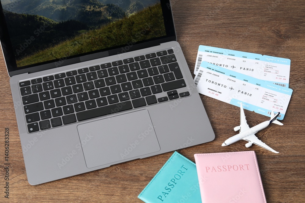 Passports, flight tickets, plane model and laptop on wooden table, above view