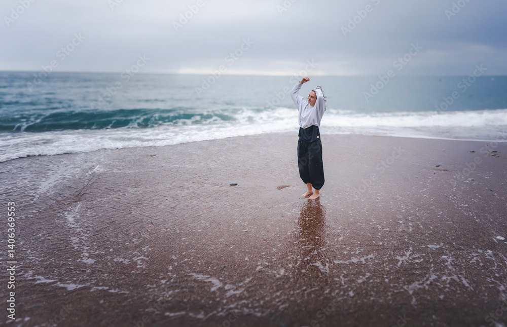 Woman dancing on sandy seashore in rainy weather, mindful movement dance meditation concept