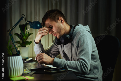 Obraz na płótnie Tired man rubs eyes while working at computer. Fatigued freelancer working late at home office. Concept of stress and mental fatigue during remote work w salonie