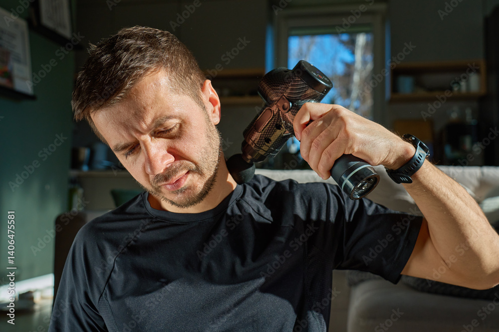 Man applies massage gun to relieve tension in neck and shoulder area. Male athlete doing self-massage therapy with percussion device for recovery after training