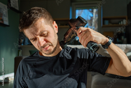 Obraz na płótnie Man applies massage gun to relieve tension in neck and shoulder area. Male athlete doing self-massage therapy with percussion device for recovery after training w salonie