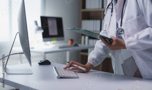 Female physician using computer keyboard and holding patient medical records in bright modern clinic or hospital office, typing medical report