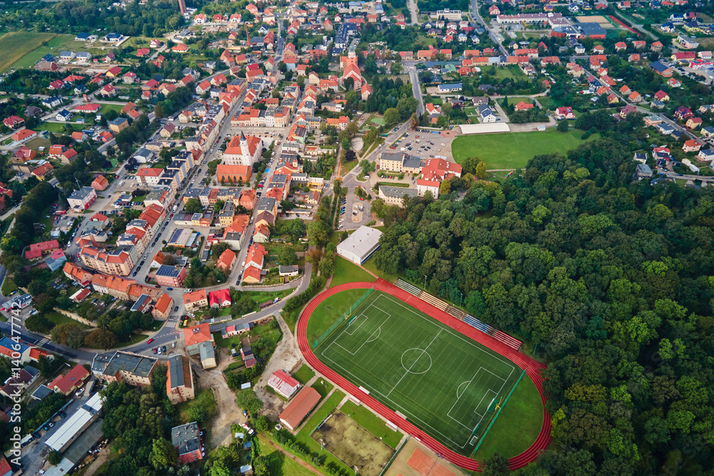 Aerial view of small European town with red roof houses, football field and green park on sunny day