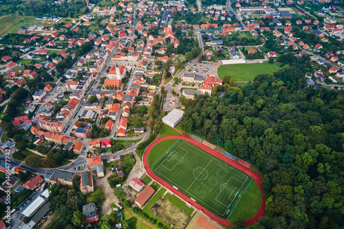 Obraz na płótnie Aerial view of small European town with red roof houses, football field and green park on sunny day w salonie