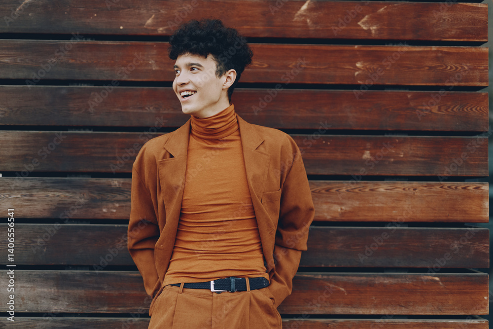 Young man in stylish brown outfit smiling against a wooden background