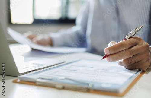 asian businessman reviewing document at office workplace with computer laptop. legal expert, professional lawyer reading and checking financial documents or insurance contract, close up shot