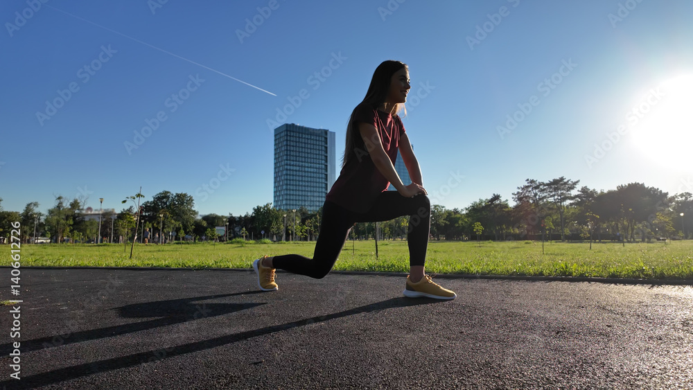 Young woman stretching after exercise and jogging in urban park during sunny summertime day..