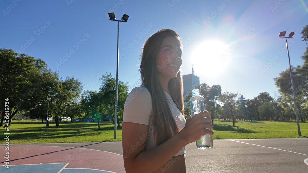 Young exhausted woman drinking water after jogging and exercise in urban park..
