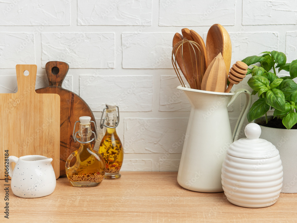 Kitchen utensils, basil plant and condiments resting on wooden countertop in front of white brick wall