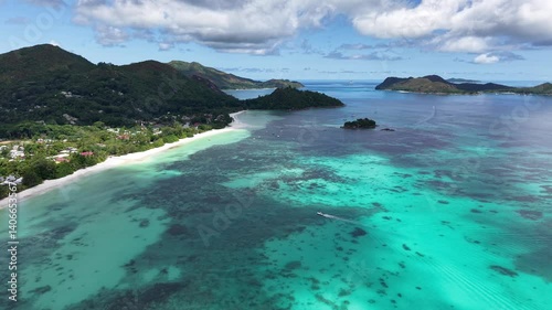 Praslin Island, Seychelles, with lush green hills, turquoise sea, and scenic tropical coastline under a clear blue sky.

