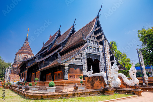 Wat Lok Moli  temple featuring a traditional wooden viharn with naga statues and an ancient brick chedi under clear blue sky, Chiang mai 
