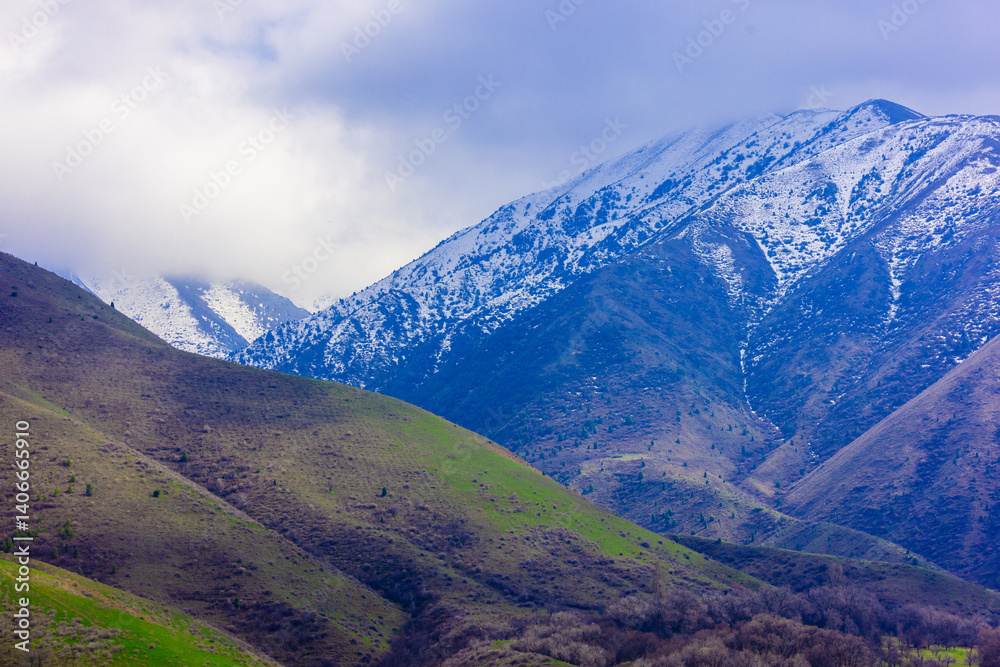Fototapeta premium Snow-capped mountain range under a cloudy sky in springtime Kyrgyzstan.