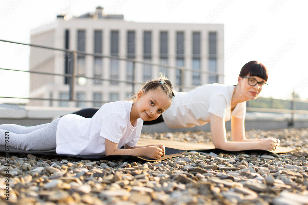 Mother and daughter practicing fitness exercises together outdoors illustrating family bonding and healthy habits. Individuals performing plank exercise in outdoor urban setting Mother and daughter practicing fitness exercises together outdoors illustrating family bonding and healthy habits. Individuals performing plank exercise in outdoor urban setting
