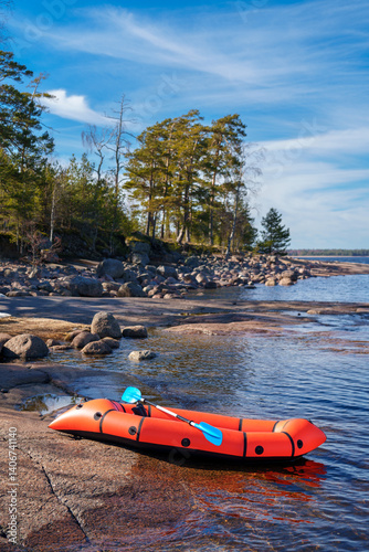 Orange packraft on the granite shore of the island. Object in focus, forest background is blurred.