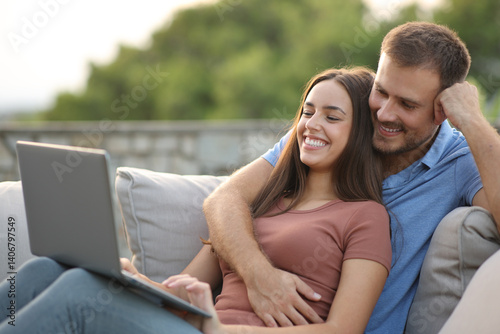 Happy couple watching online videos on laptop in a terrace photo