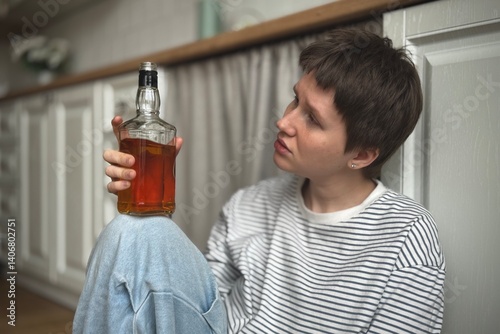 Young depressed woman is drinking alcohol and suffering at the kitchen