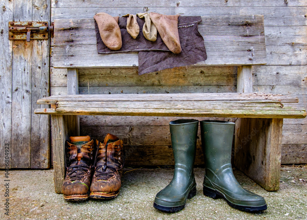 Worn boots and rain gear on a rustic bench beside a weathered wooden door at a farm in the countryside showcasing rural lifestyle