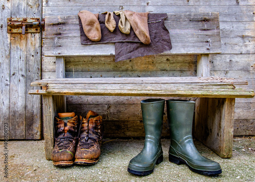 Obraz na płótnie Worn boots and rain gear on a rustic bench beside a weathered wooden door at a farm in the countryside showcasing rural lifestyle w salonie
