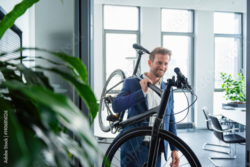 Businessman in a modern office carrying a bike and smiling
