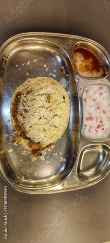 a serving of biryani on a stainless steel compartmental plate