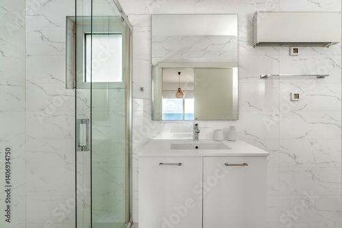 Bright white bathroom with wall-mounted sink, mirror reflecting seaside view, enclosed glass shower, marble tiles, and modern light fixture. Clean, airy, and contemporary space.