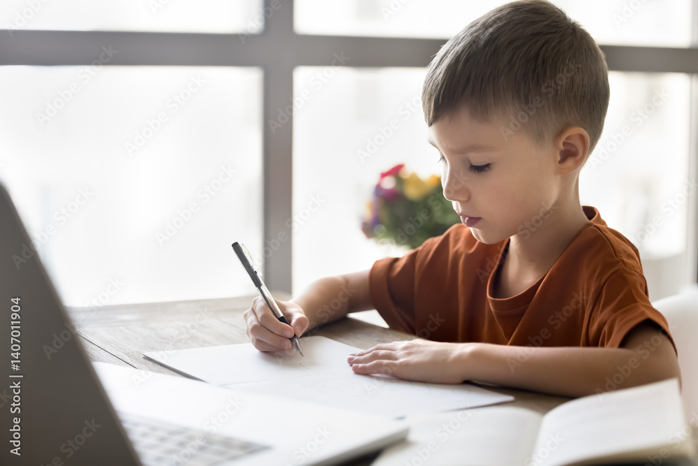 Diligent remote student. Portrait busy junior school age boy sit at home desk before notebook screen writing in copybook doing homework taking notes after teacher in online virtual class. Copy space Diligent remote student. Portrait busy junior school age boy sit at home desk before notebook screen writing in copybook doing homework taking notes after teacher in online virtual class. Copy space