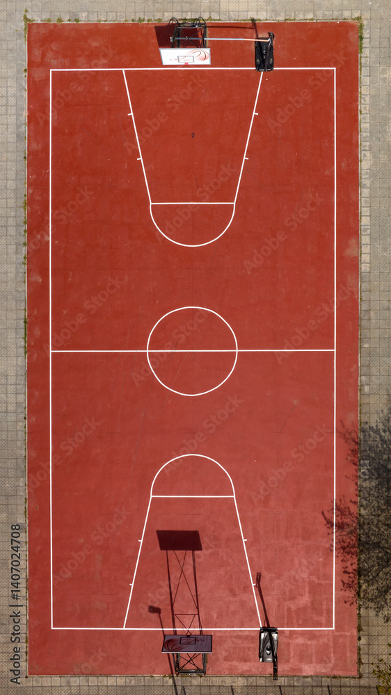 Aerial zenithal view of an empty basketball court. The playground has two hoops and a red floor.
