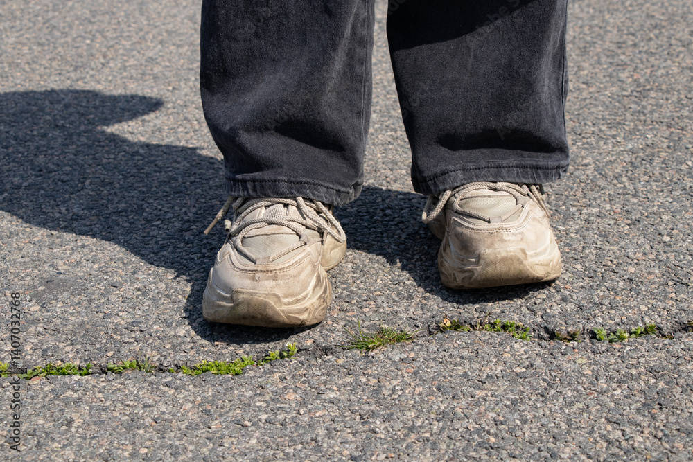 Child's feet in dirty sneakers on asphalt near a crack with sprouted grass in the spring in the sun Child's feet in dirty sneakers on asphalt near a crack with sprouted grass in the spring in the sun